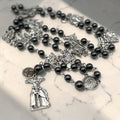 Close-up Way of the Cross chaplet with glossy dark gray hematite beads, silver station medals, Holy Face of Jesus centerpiece, and crucifix