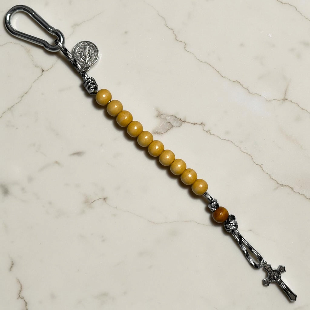 Saint Benedict decade rosary with beige wood beads, tan Our Father bead, black and white paracord, carabiner, and silver-tone crucifix