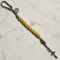 Saint Benedict decade rosary with beige wood beads, tan Our Father bead, black and white paracord, carabiner, and silver-tone crucifix