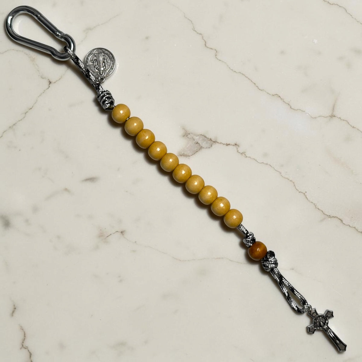 Saint Benedict decade rosary with beige wood beads, tan Our Father bead, black and white paracord, carabiner, and silver-tone crucifix