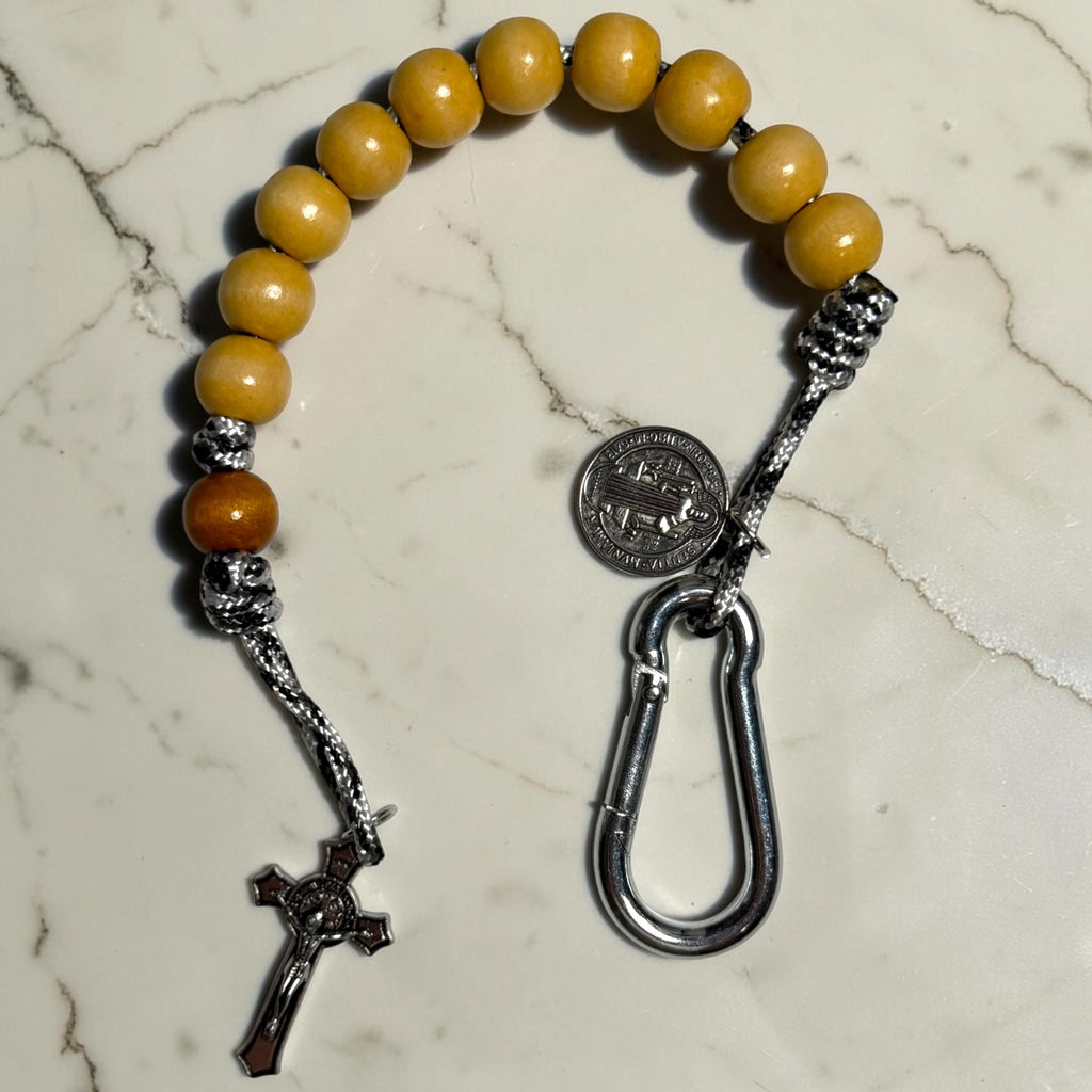 Close-up of Saint Benedict decade rosary with beige wood beads, tan Our Father bead, black and white paracord, carabiner, medal, and crucifix