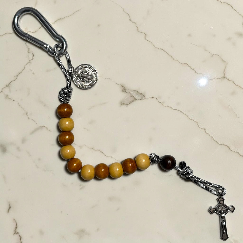 Saint Benedict decade rosary with alternating beige and warm brown wood beads, dark brown Our Father bead, black and white paracord, carabiner, medal, and crucifix