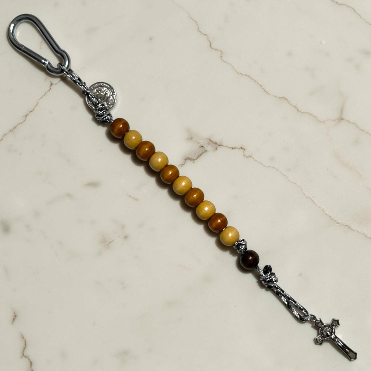 Full-length Saint Benedict decade rosary with alternating beige and brown wood beads, black and white paracord, dark brown Our Father bead, carabiner, medal, and crucifix