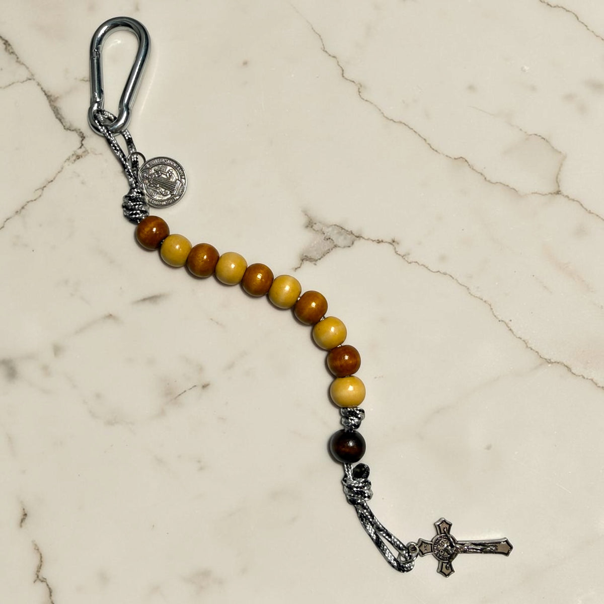 Saint Benedict decade rosary with alternating beige and brown wood beads, dark brown Our Father bead, black and white paracord, silver-tone carabiner, medal, and crucifix