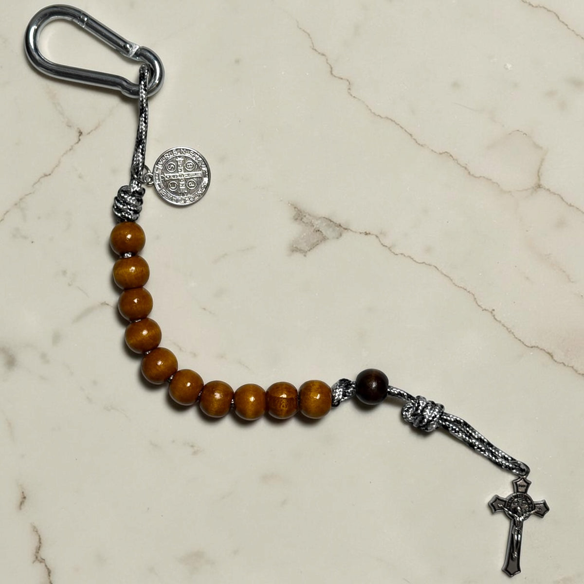 Full-length Saint Benedict decade rosary with warm brown wood beads, dark brown Our Father bead, black and white paracord, carabiner, medal, and crucifix