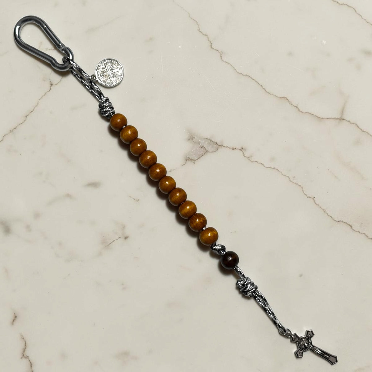 Saint Benedict decade rosary with warm brown wood beads, dark brown Our Father bead, black and white paracord, silver-tone medal, carabiner, and crucifix