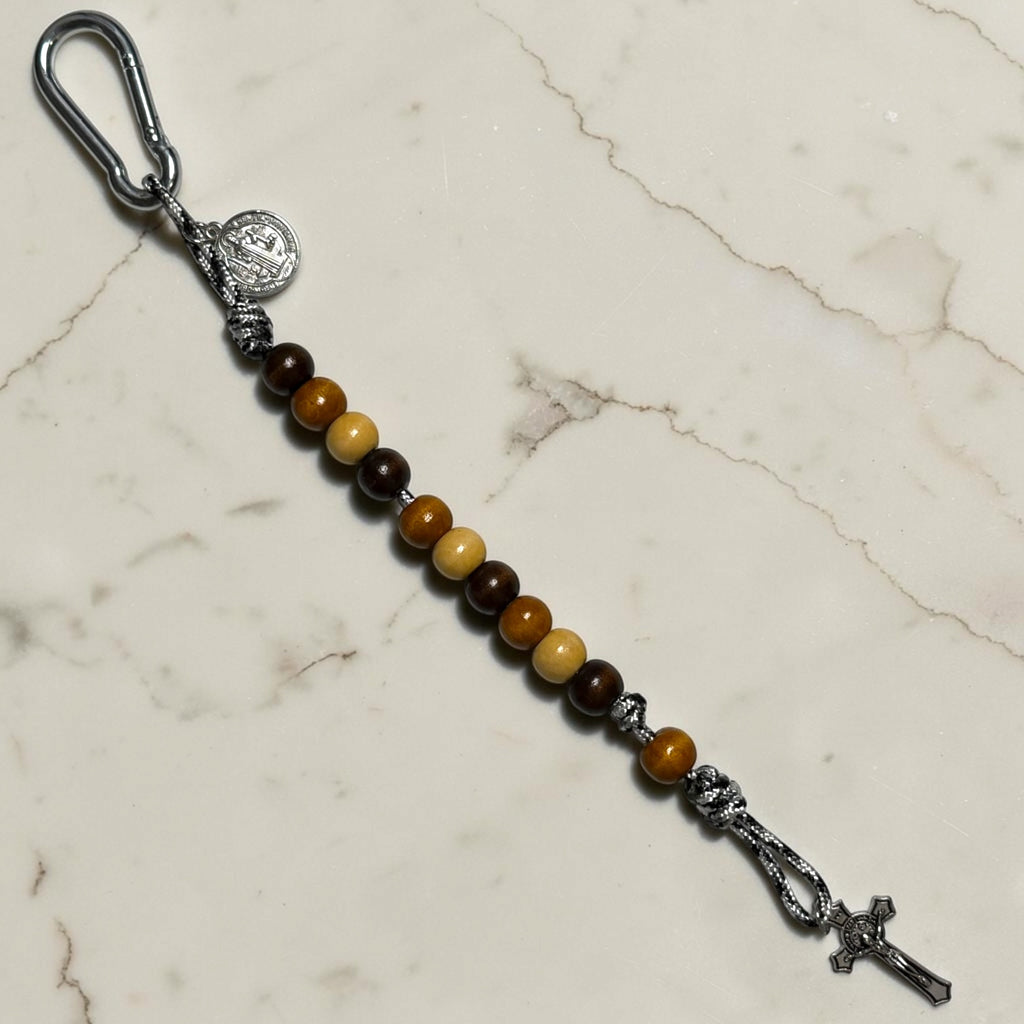 Full-length Saint Benedict decade rosary with mixed dark brown, warm brown, and beige wood beads, black and white paracord, brown Our Father bead, carabiner, medal, and crucifix