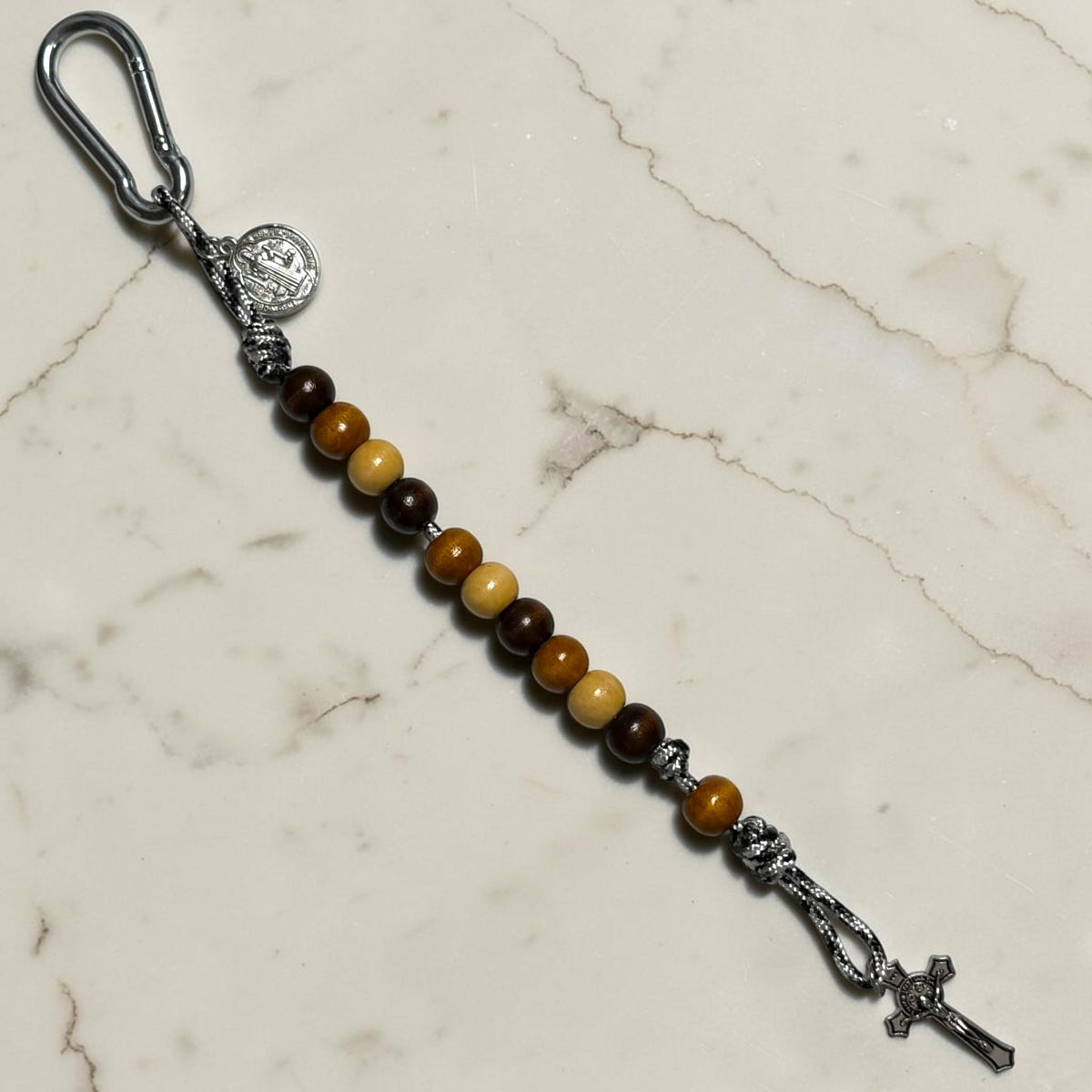 Full-length Saint Benedict decade rosary with mixed dark brown, warm brown, and beige wood beads, black and white paracord, brown Our Father bead, carabiner, medal, and crucifix