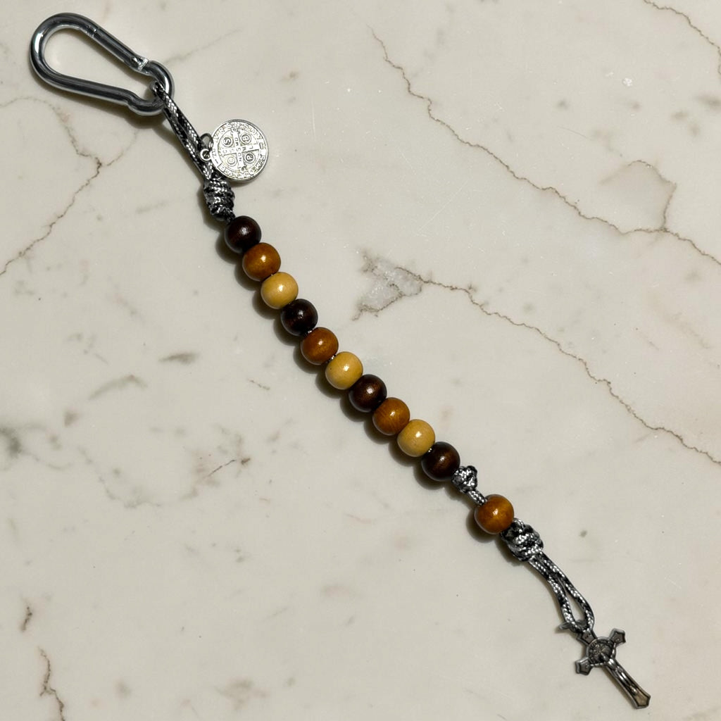 Saint Benedict decade rosary with patterned dark brown, warm brown, and beige wood beads, brown Our Father bead, black and white paracord, medal, carabiner, and crucifix