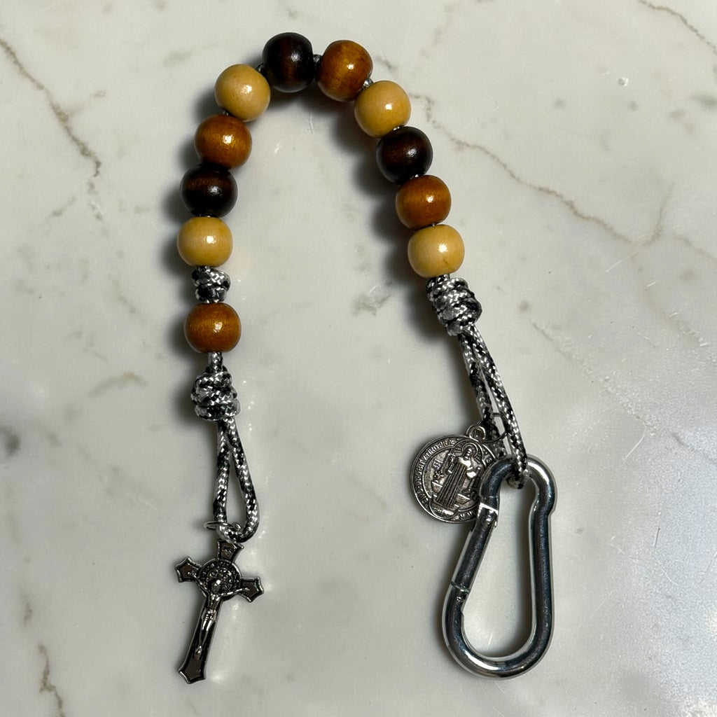 Saint Benedict decade rosary with alternating beige, medium brown, and dark brown wood beads, warm brown Our Father bead, black and white paracord, carabiner, medal, and crucifix