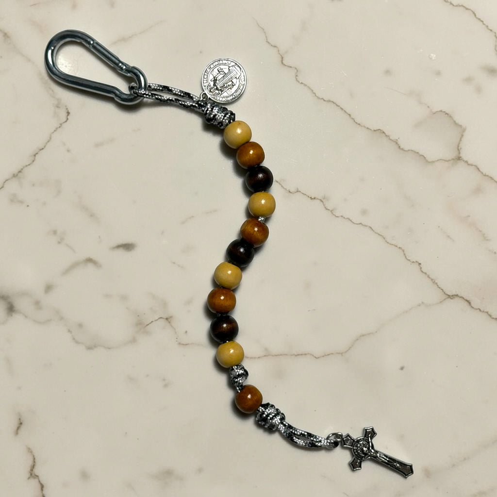 Saint Benedict decade rosary with beige, medium brown, and dark brown wood beads, warm brown Our Father bead, black and white paracord, silver-tone carabiner, medal, and crucifix