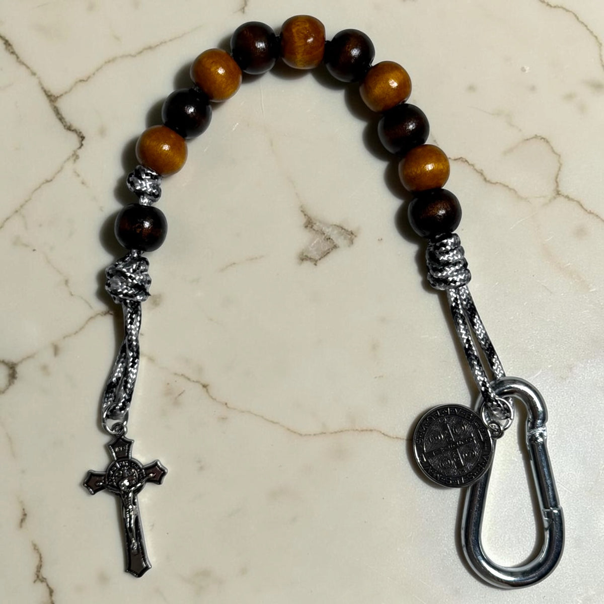 Saint Benedict decade rosary with alternating dark brown and warm brown wood beads, dark brown Our Father bead, black and white paracord, carabiner, medal, and crucifix