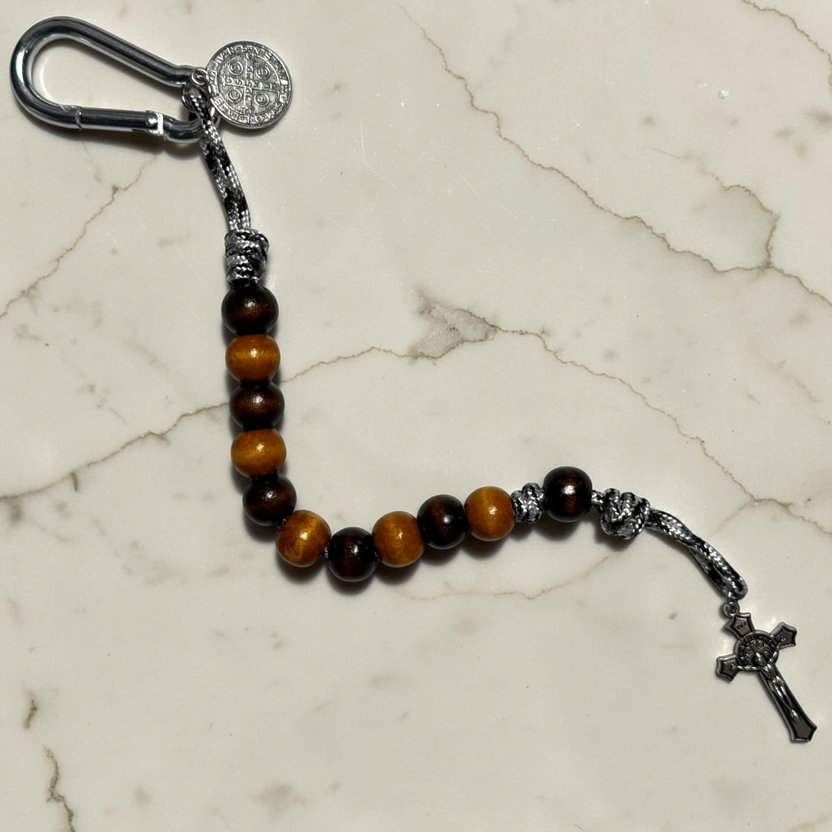 Saint Benedict decade rosary with alternating dark brown and warm brown wood beads, dark brown Our Father bead, black and white paracord, silver-tone carabiner, medal, and crucifix