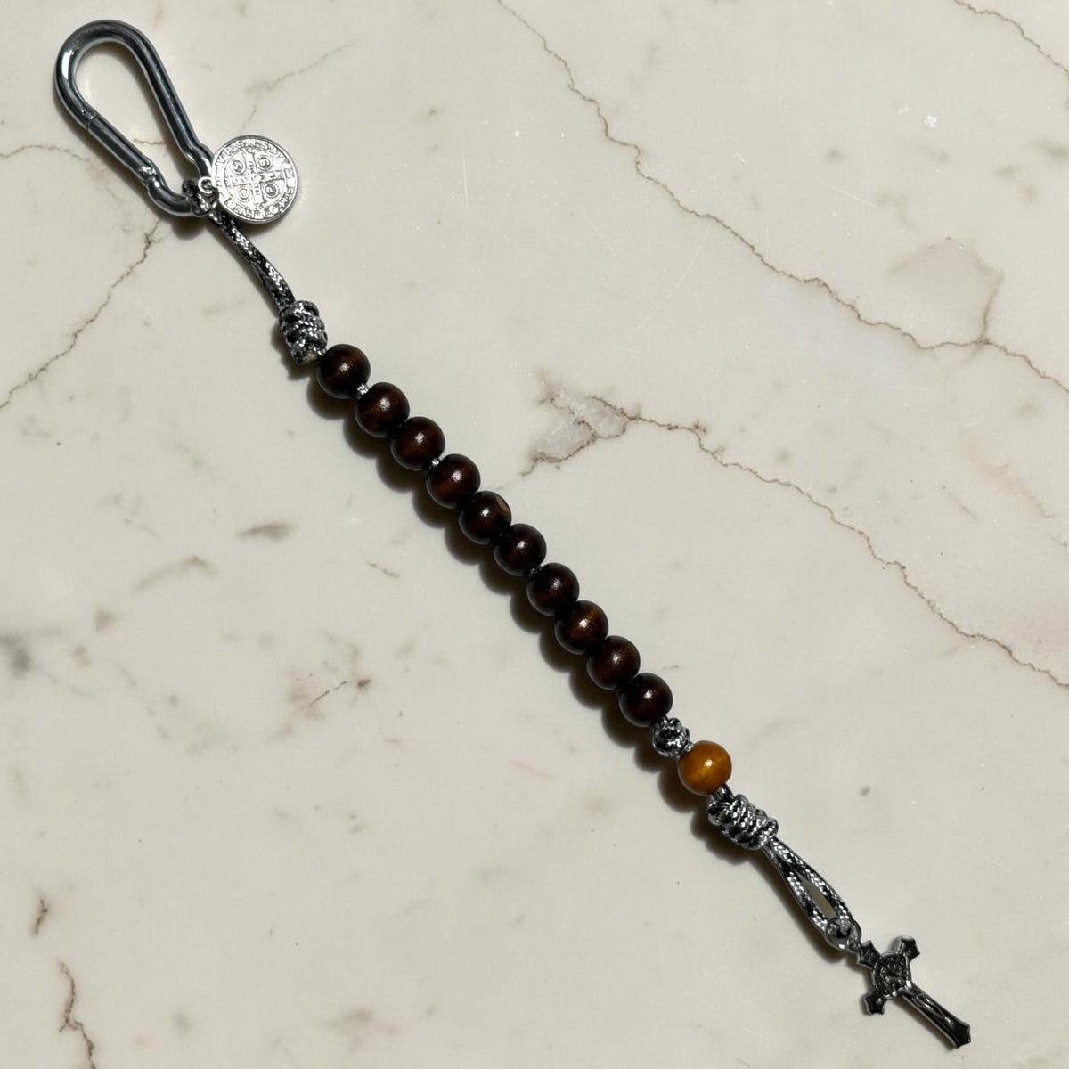 Saint Benedict decade rosary with dark brown wood beads, tan Our Father bead, black and white paracord, carabiner, medal, and crucifix