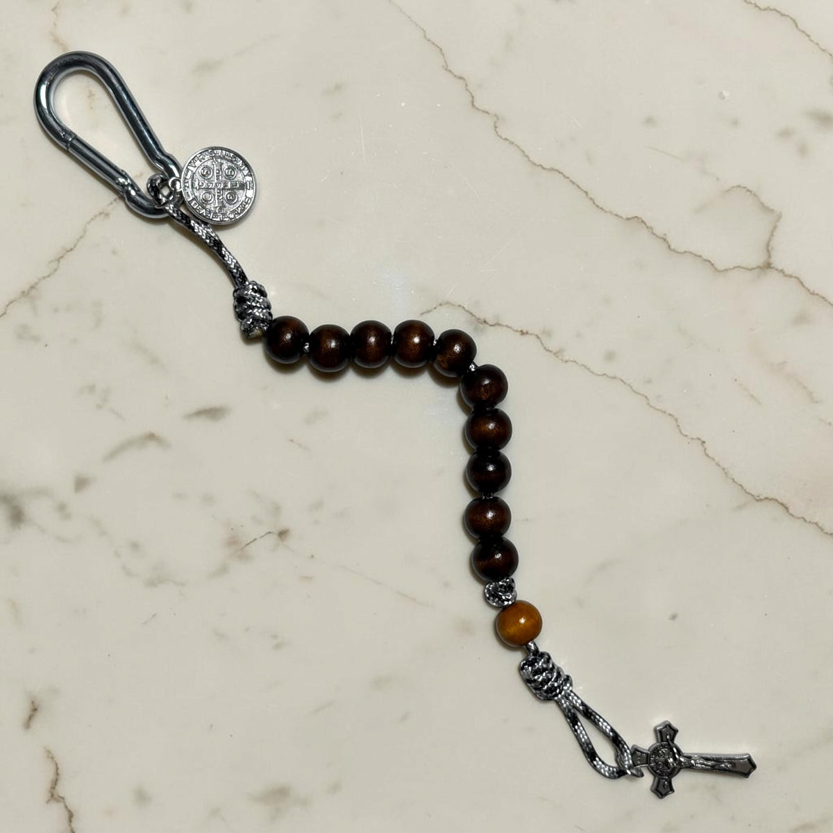 Full-length Saint Benedict decade rosary with dark brown wood beads, tan Our Father bead, black and white paracord, carabiner, medal, and crucifix