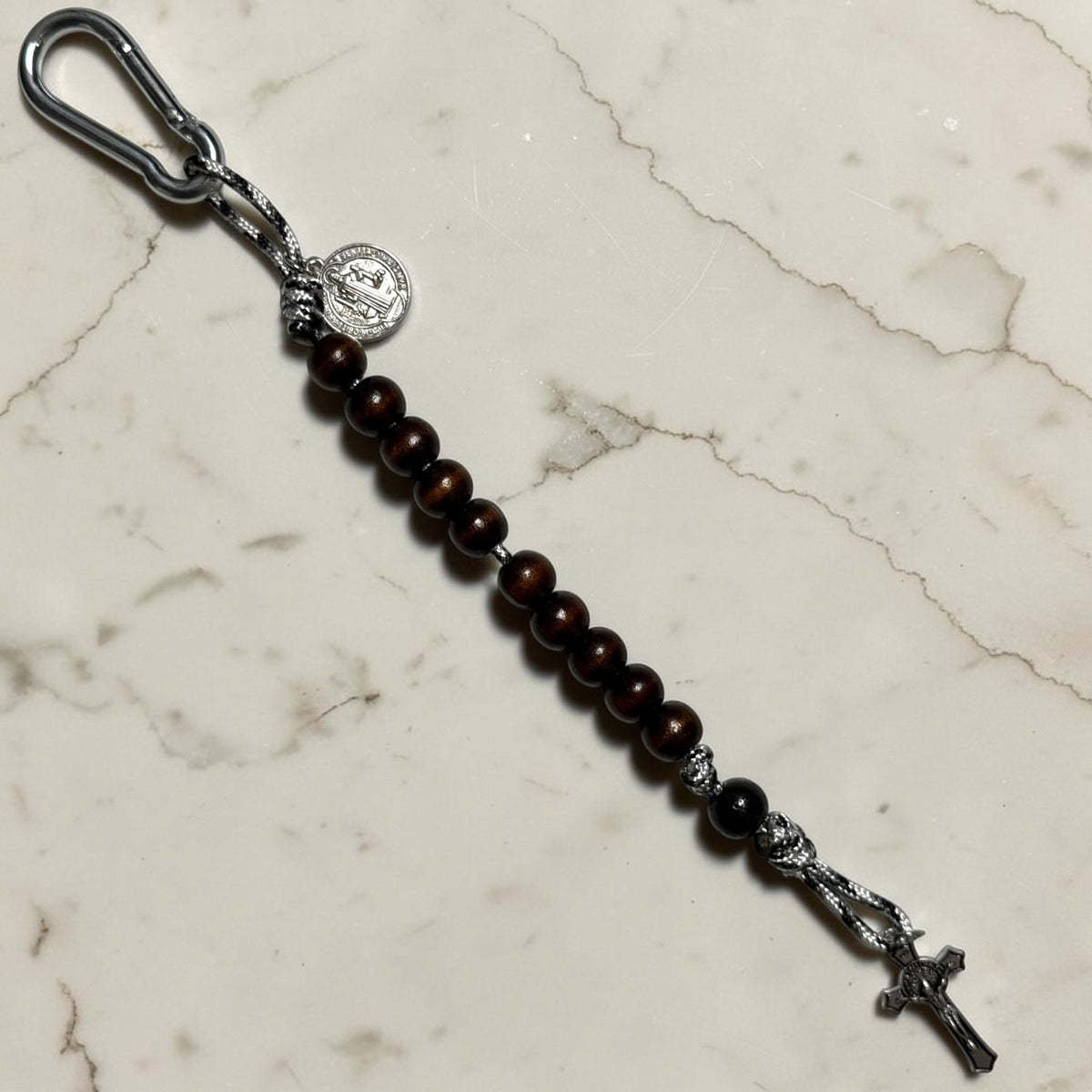 Saint Benedict decade rosary with dark brown wood beads, black Our Father bead, black and white paracord, carabiner, medal, and crucifix
