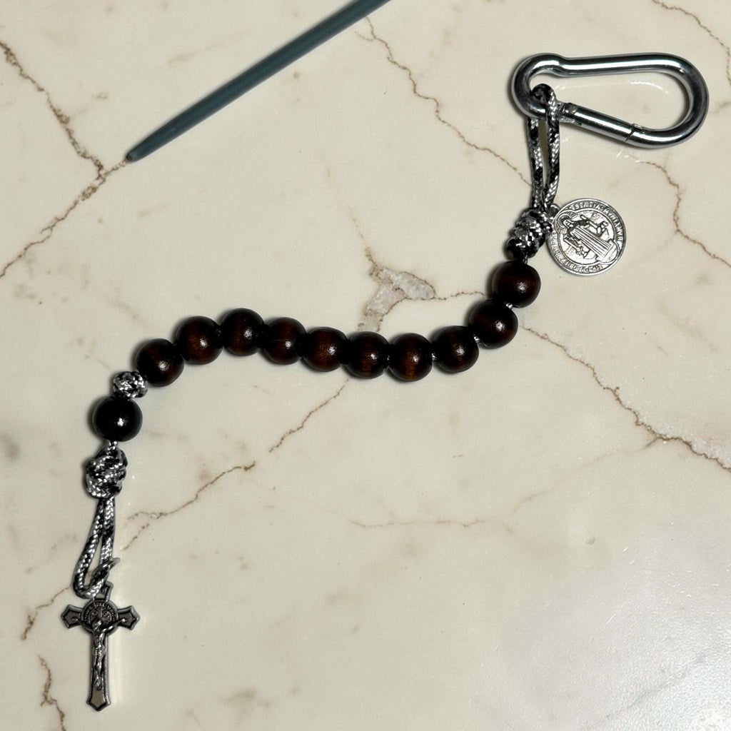 Full-length Saint Benedict decade rosary with dark brown wood beads, black Our Father bead, black and white paracord, carabiner, medal, and crucifix