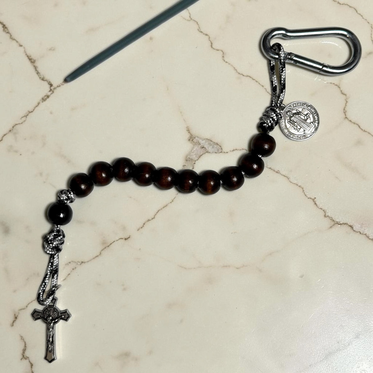 Full-length Saint Benedict decade rosary with dark brown wood beads, black Our Father bead, black and white paracord, carabiner, medal, and crucifix
