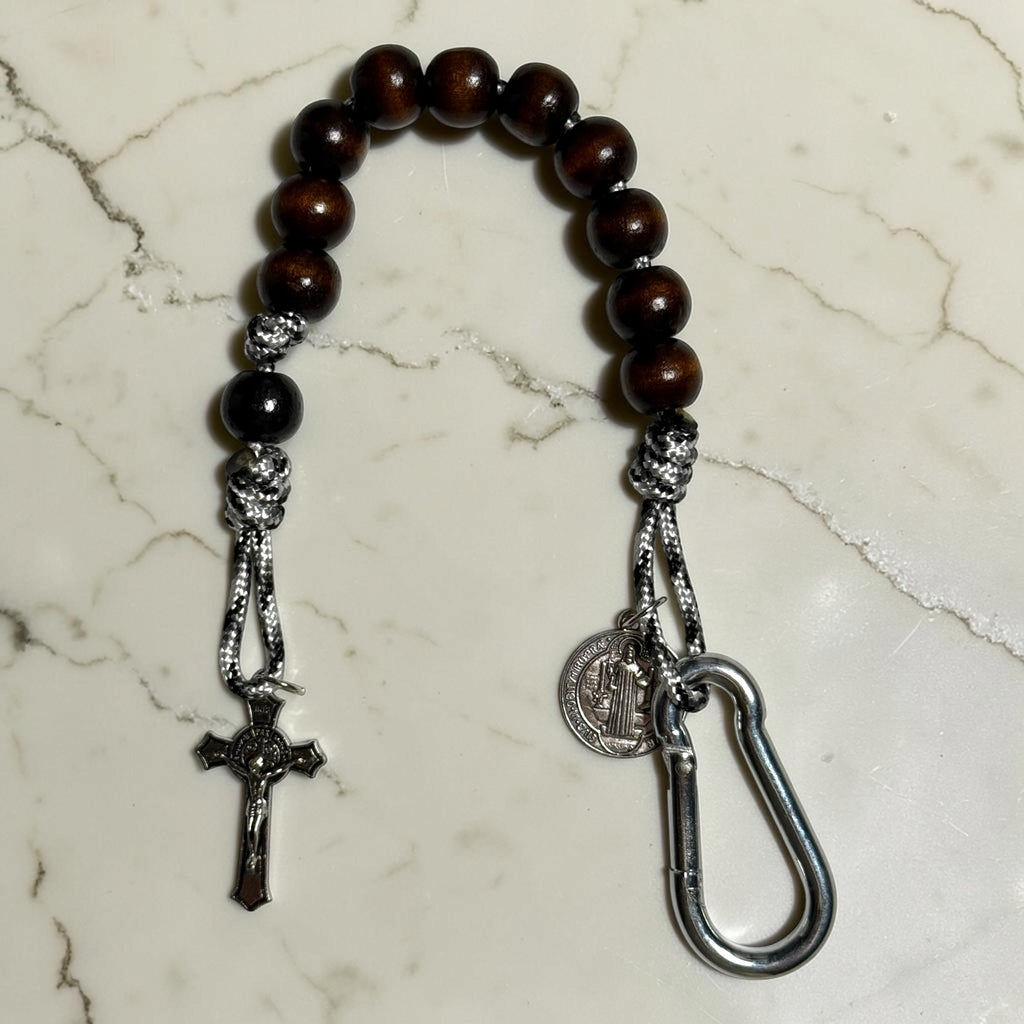 Saint Benedict decade rosary with dark brown wood beads, black Our Father bead, black and white paracord, silver-tone carabiner, medal, and crucifix