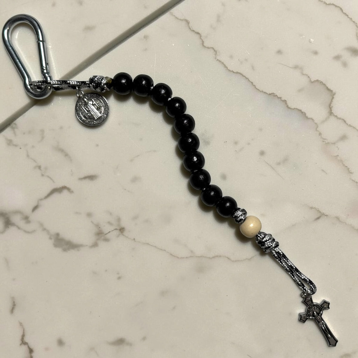 Saint Benedict decade rosary with black wood beads, white Our Father bead, black and white paracord, carabiner, medal, and crucifix