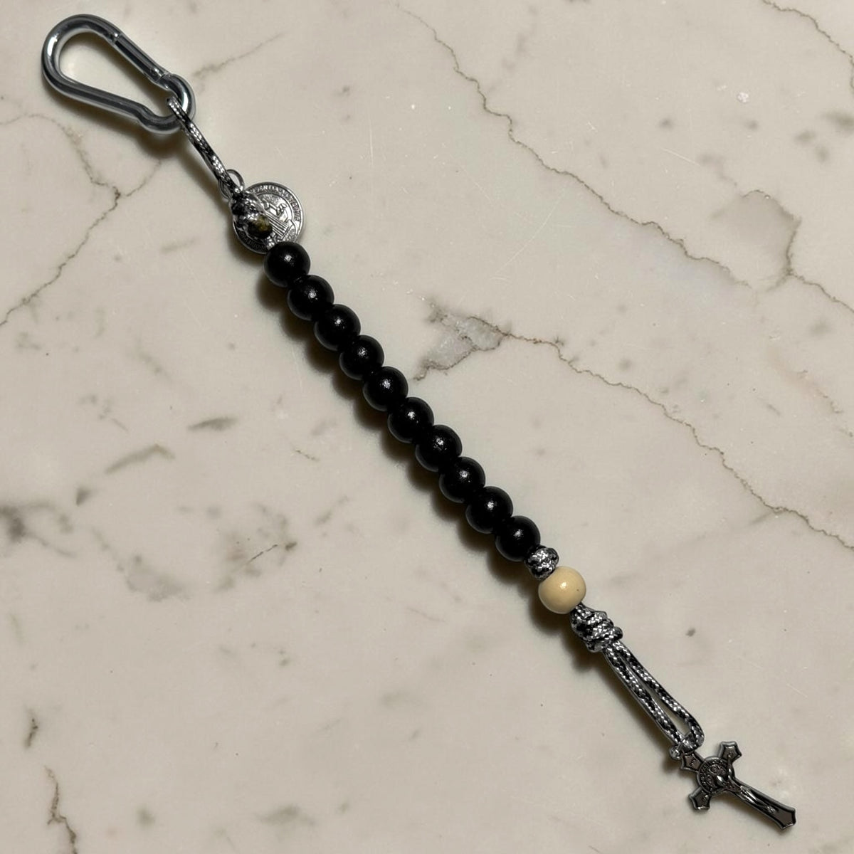 Full-length Saint Benedict decade rosary with black wood beads, white Our Father bead, black and white paracord, silver-tone carabiner, medal, and crucifix