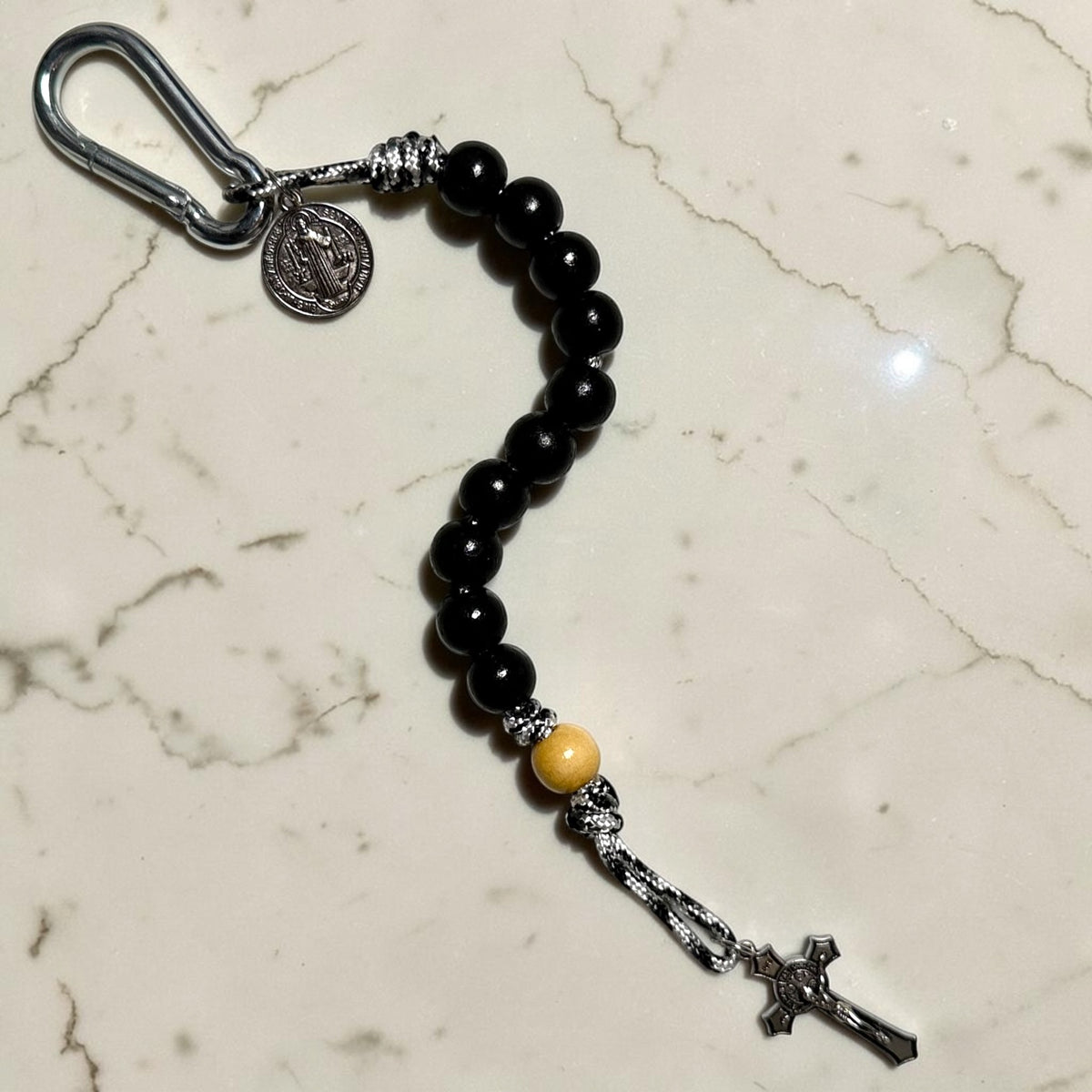 Saint Benedict decade rosary with black wood beads, beige Our Father bead, black and white paracord, carabiner, medal, and crucifix