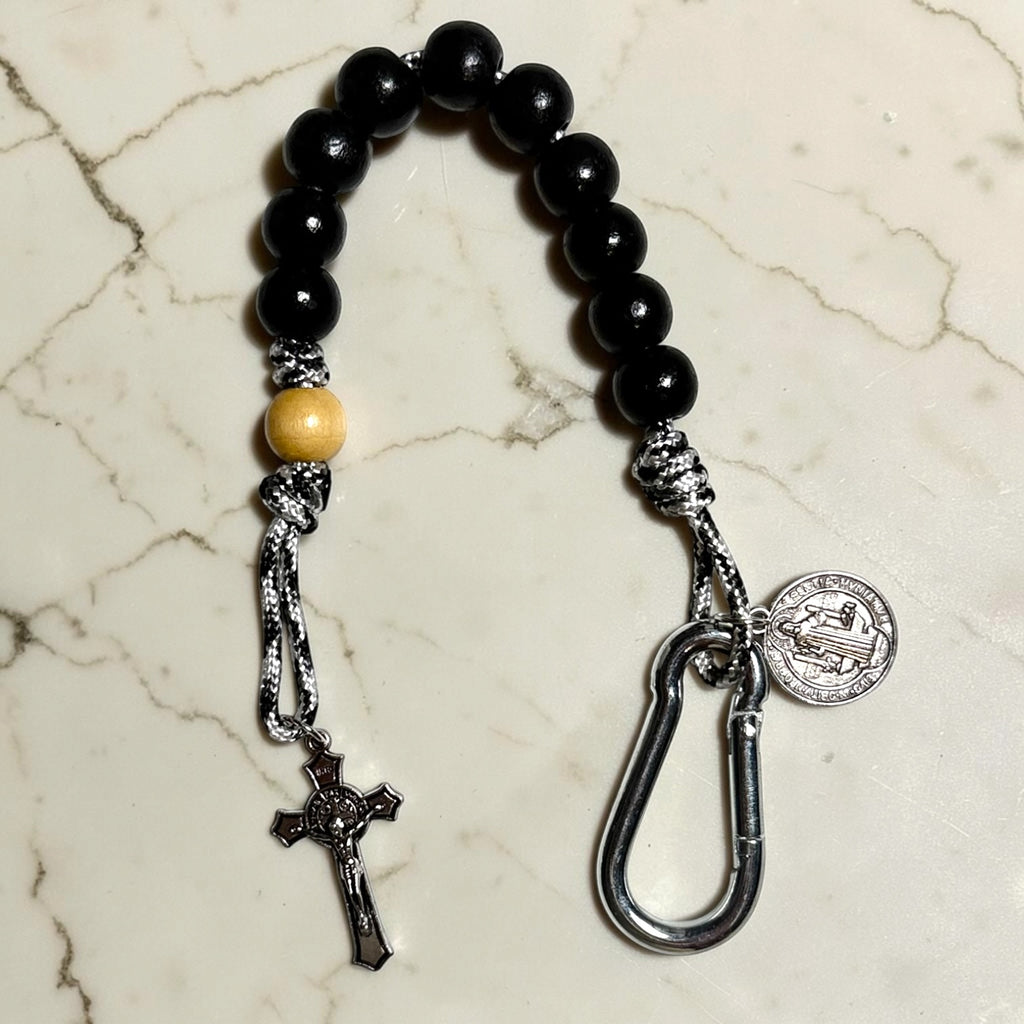 Saint Benedict decade rosary with black wood beads, beige Our Father bead, black and white paracord, silver-tone carabiner, medal, and crucifix