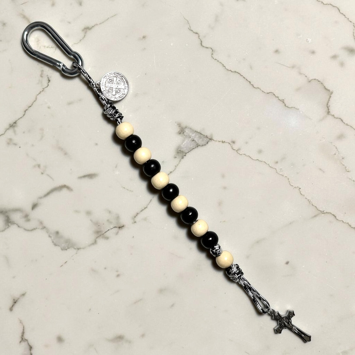 Saint Benedict decade rosary with alternating black and ivory wood beads, ivory Our Father bead, black and white paracord, carabiner, medal, and crucifix