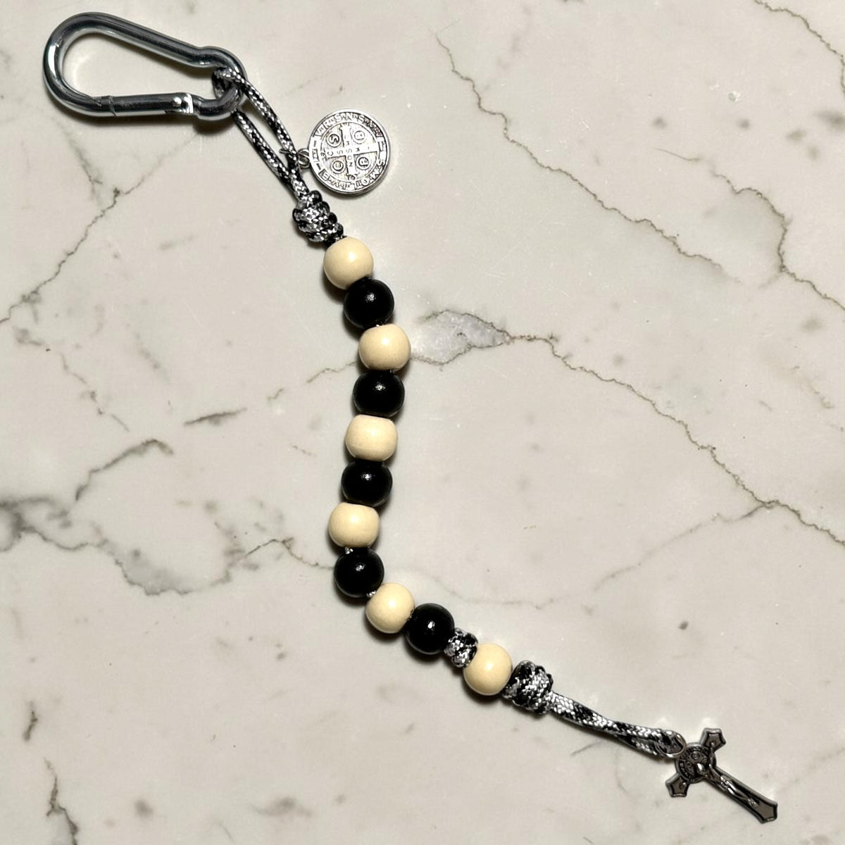 Full-length Saint Benedict decade rosary with alternating black and ivory wood beads, ivory Our Father bead, black and white paracord, carabiner, medal, and crucifix