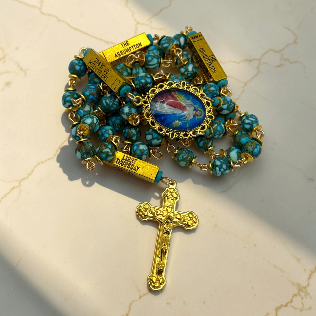 Close-up of gold and turquoise Divine Mercy guided mystery rosary with turquoise stone-look beads, engraved gold mystery bars, Divine Mercy centerpiece, and gold crucifix