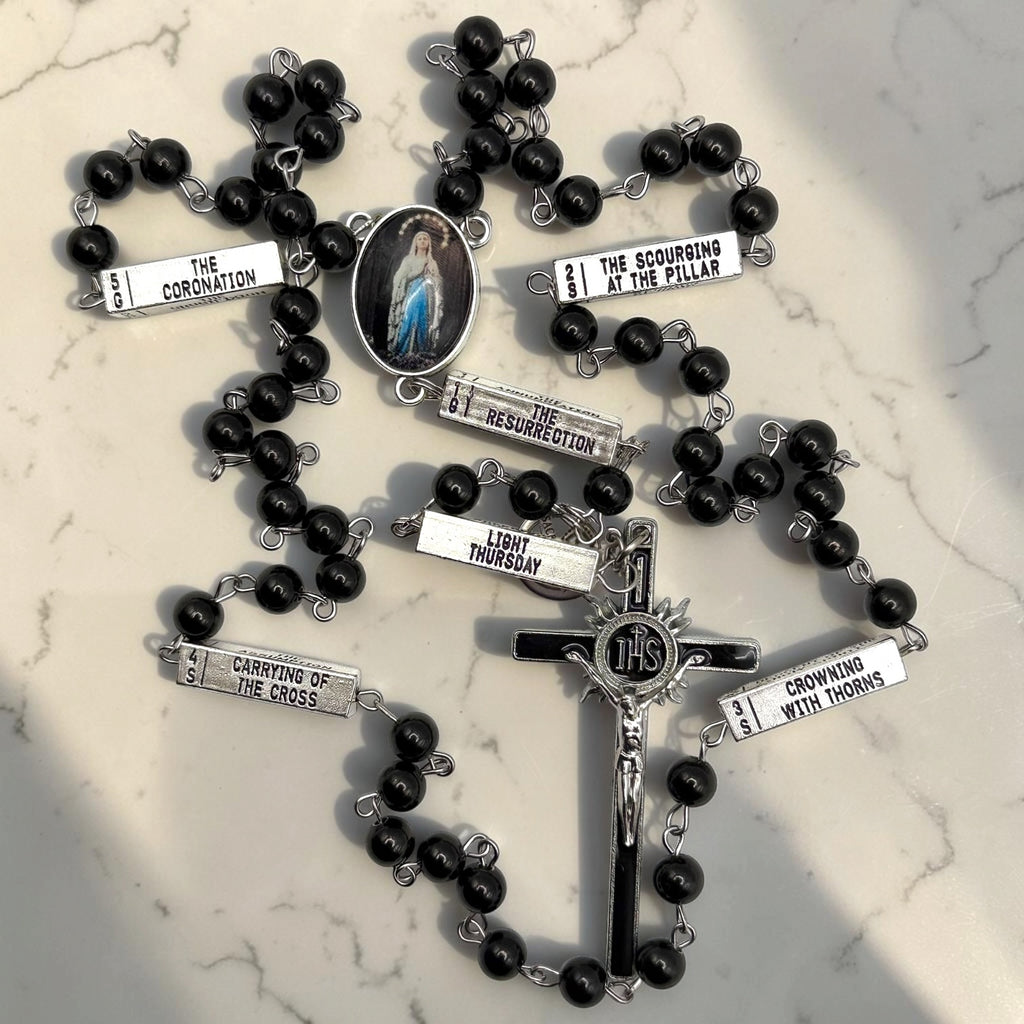 Close-up black and silver Guided Mystery Rosary with Our Lady of Lourdes centerpiece, engraved mystery bars, glossy black beads, and IHS crucifix