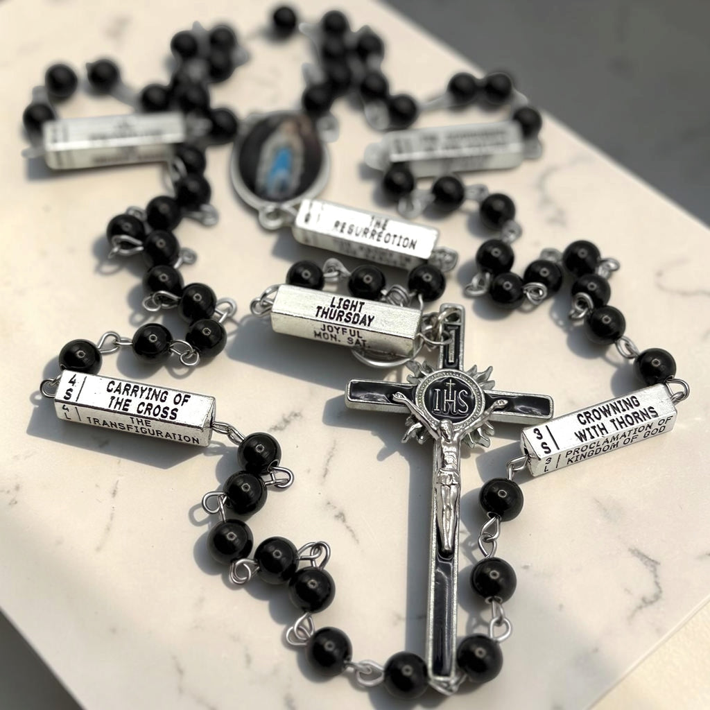 Detailed black and silver Guided Mystery Rosary showing engraved mystery bars, black beads, Our Lady of Lourdes centerpiece, and IHS crucifix
