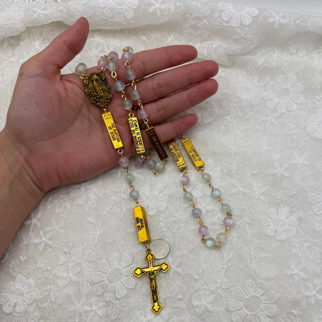 Pastel glow rosary displayed in hand with gold crucifix