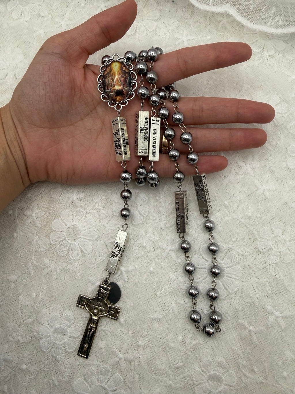 Silver Nativity and hematite rosary held in hand for scale