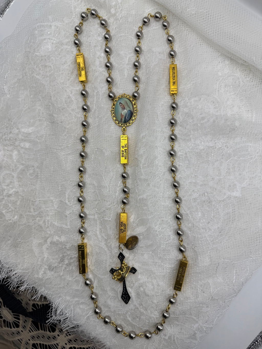 Silver and gold Marian rosary laid out to show the beads and crucifix