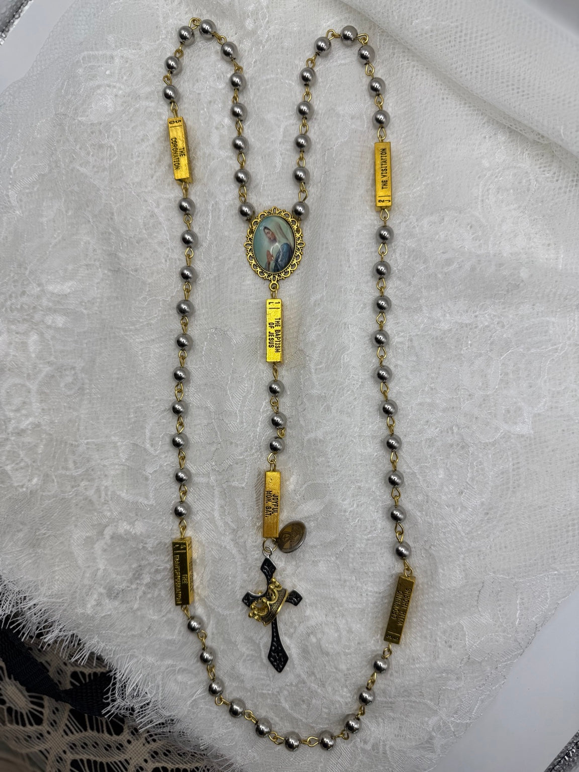 Silver and gold Marian rosary laid out to show the beads and crucifix