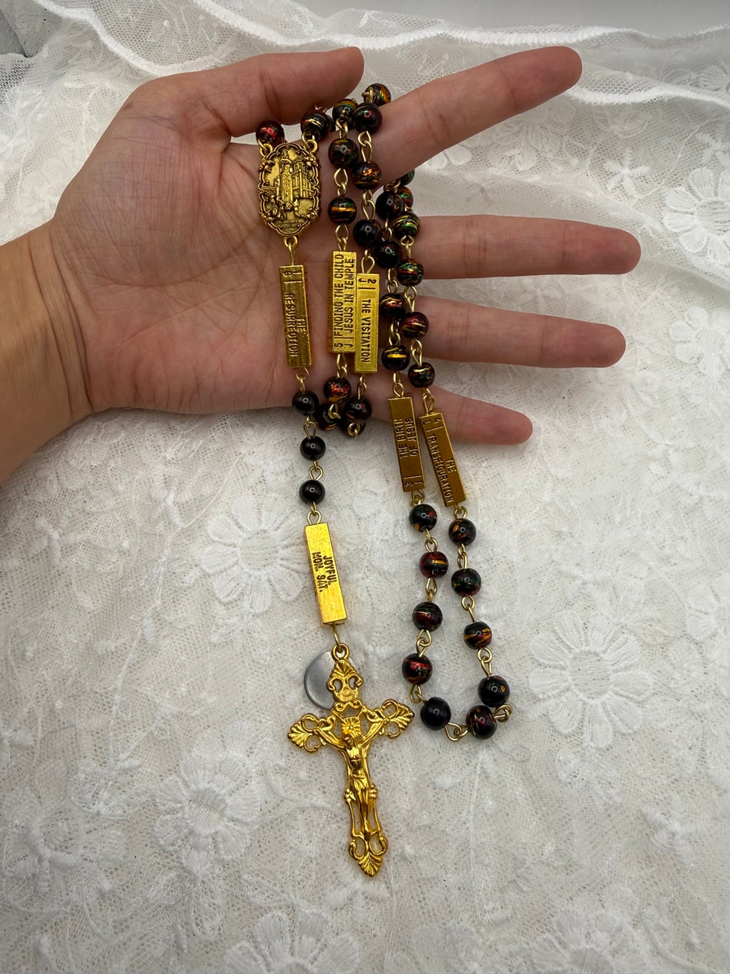 Black multicolor gold rosary held in hand