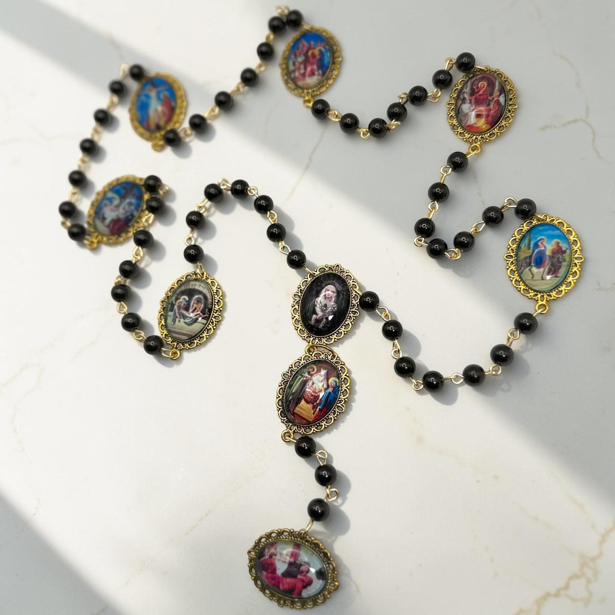 Our Lady of Sorrows chaplet laid out with black beads, gold-tone links, and glass meditation images