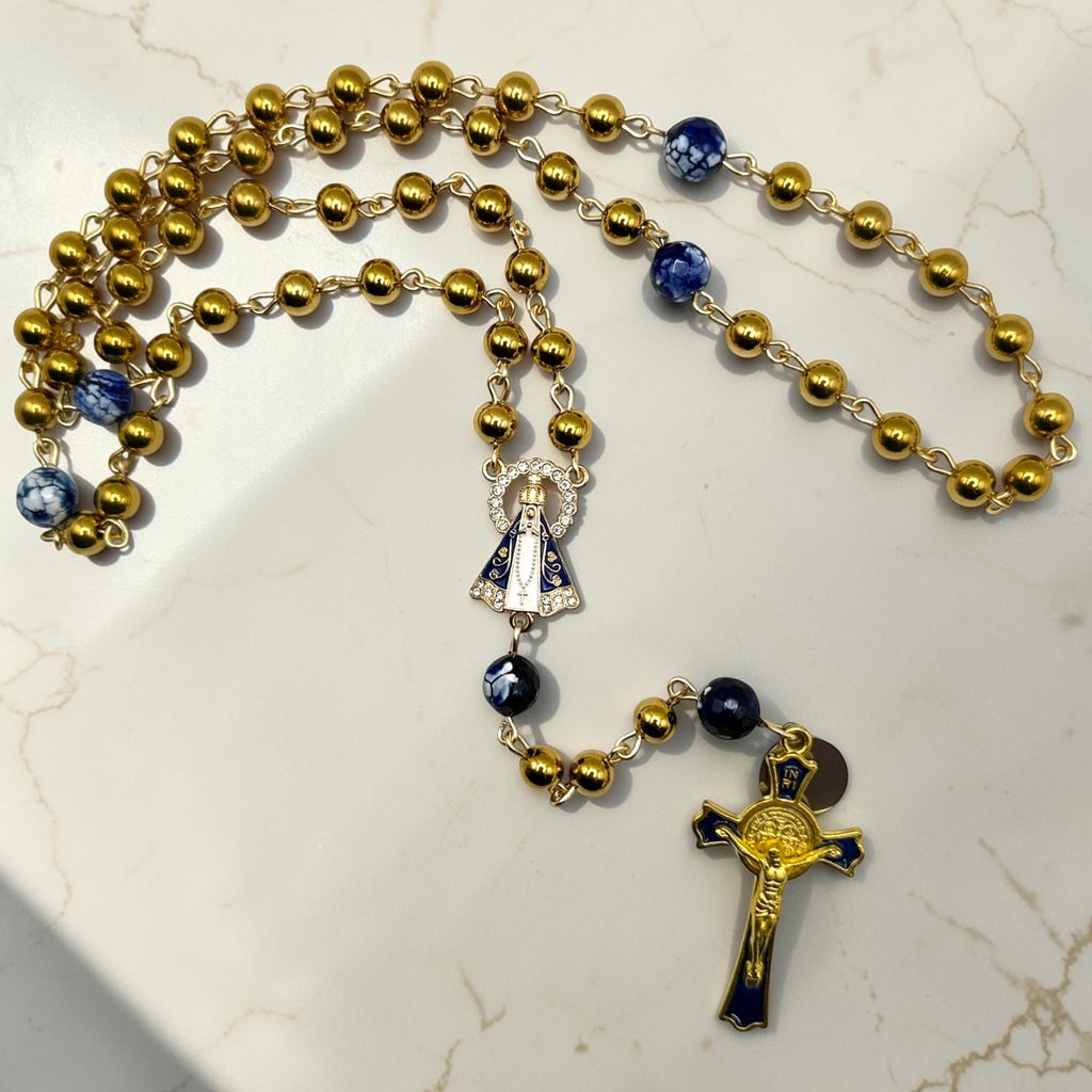 Gold and royal blue Our Lady Aparecida rosary arranged on a light marble surface