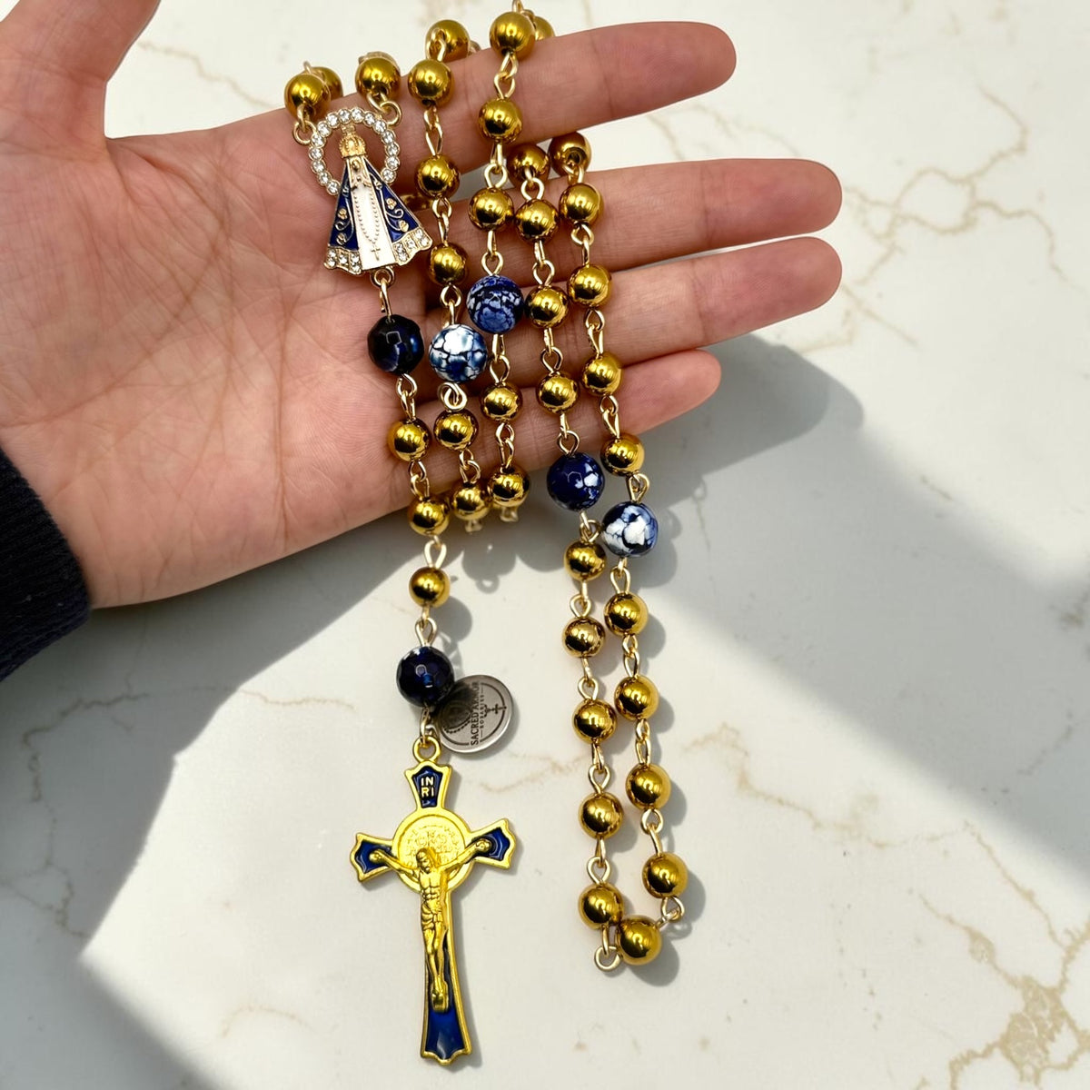 Handheld gold and royal blue Our Lady Aparecida rosary showing centerpiece, beads, and crucifix