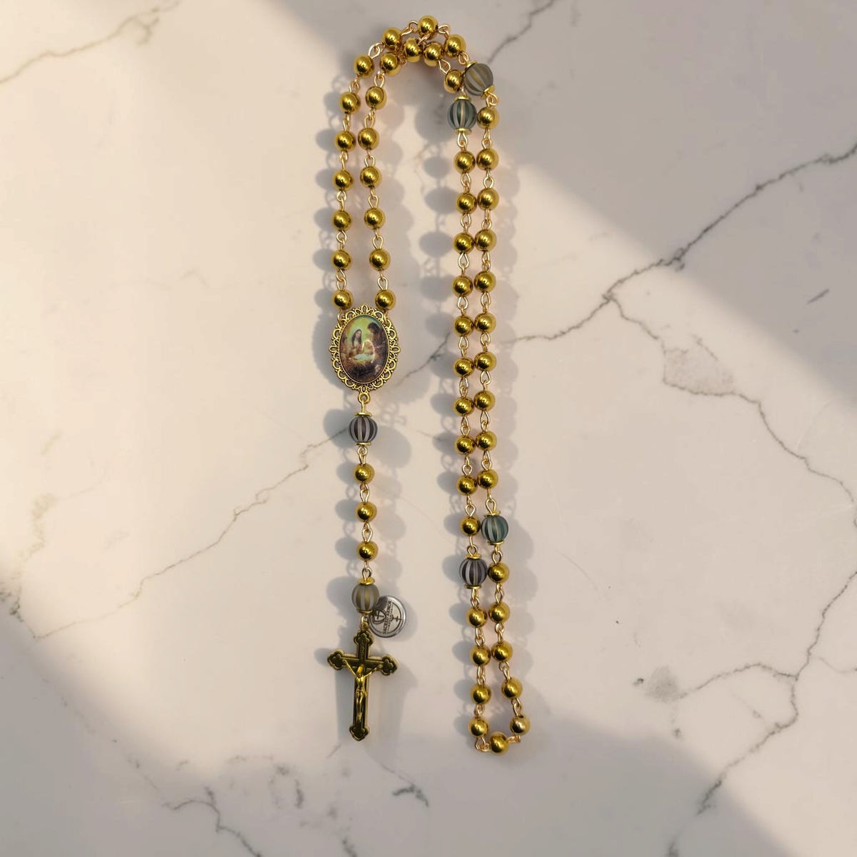 Gold Holy Family rosary with shiny gold-tone beads, striped accent Our Father beads, Holy Family centerpiece, and gold-tone crucifix