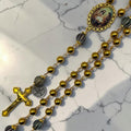 Detailed gold Holy Family rosary showing striped accent Our Father beads, Holy Family centerpiece, Sacred Armor medal, and crucifix
