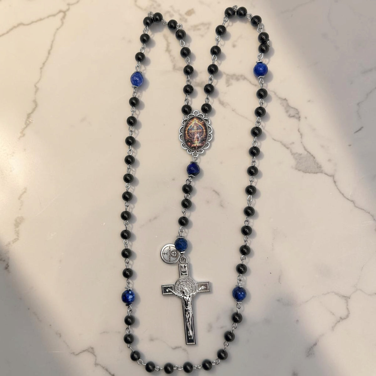 Black and blue St. Benedict rosary with glossy black beads, deep blue faceted stone accent beads, St. Benedict centerpiece, silver-tone chain, and St. Benedict crucifix