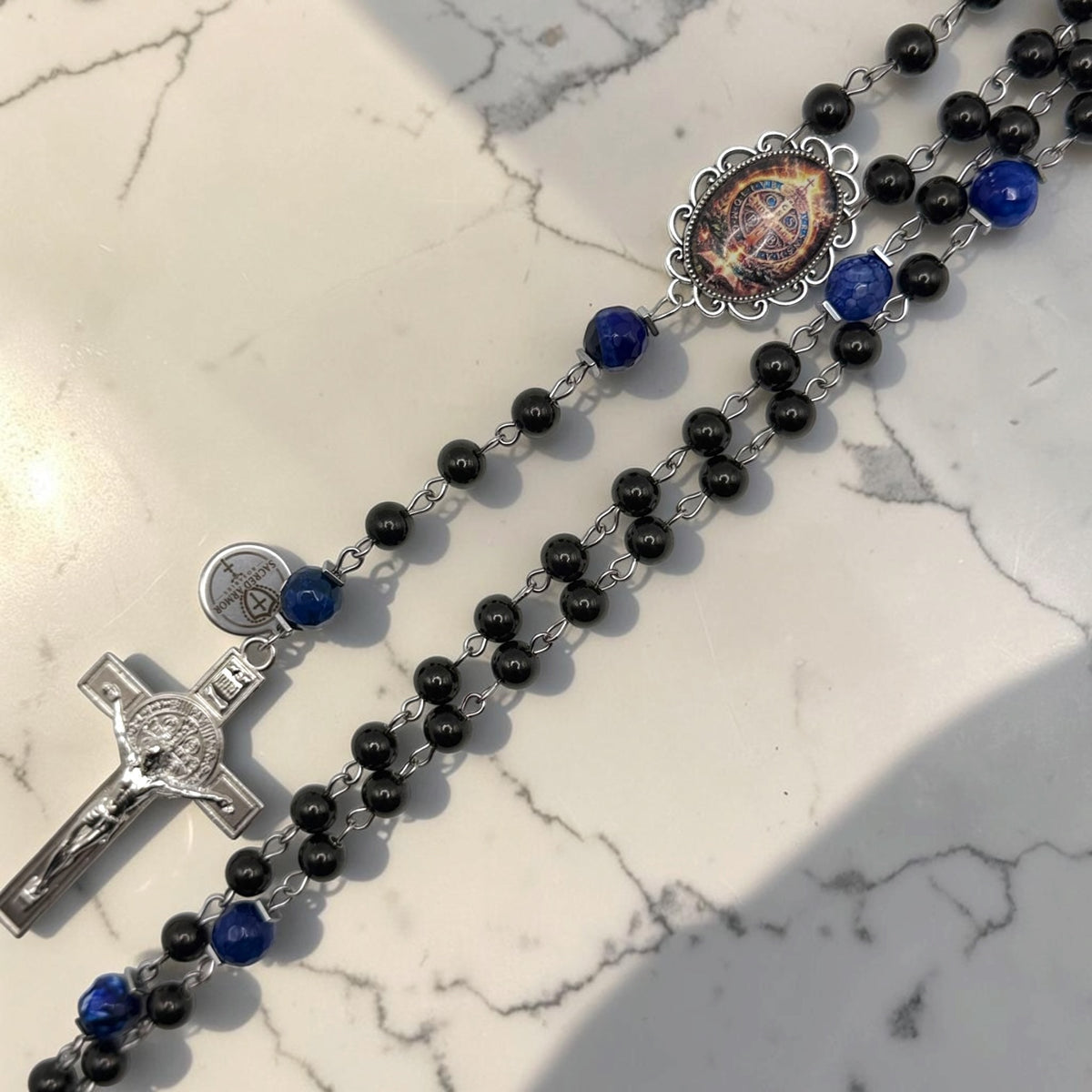 Close-up black and blue St. Benedict rosary with deep blue faceted accent beads, ornate St. Benedict centerpiece, Sacred Armor medal, and silver-tone crucifix