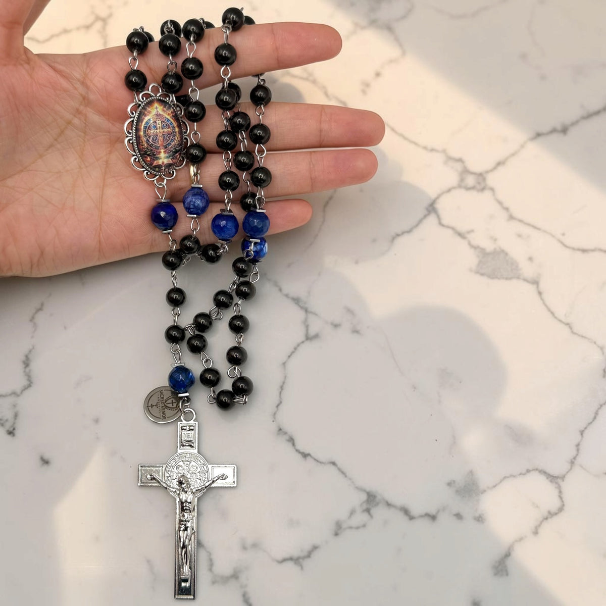 Hand-held black and blue St. Benedict rosary with glossy black beads, deep blue faceted stone accent beads, ornate St. Benedict centerpiece, Sacred Armor medal, and silver-tone crucifix