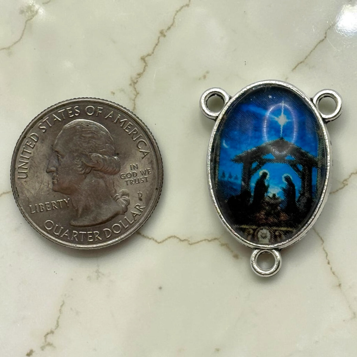 Blue Nativity glass cabochon rosary centerpiece shown beside a quarter for scale