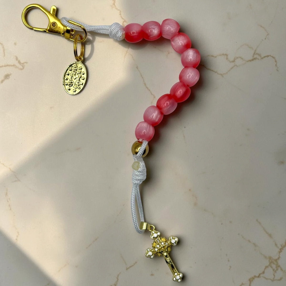 Pink and red decade rosary with white cord, gold-tone hardware, Marian medal, and crystal crucifix