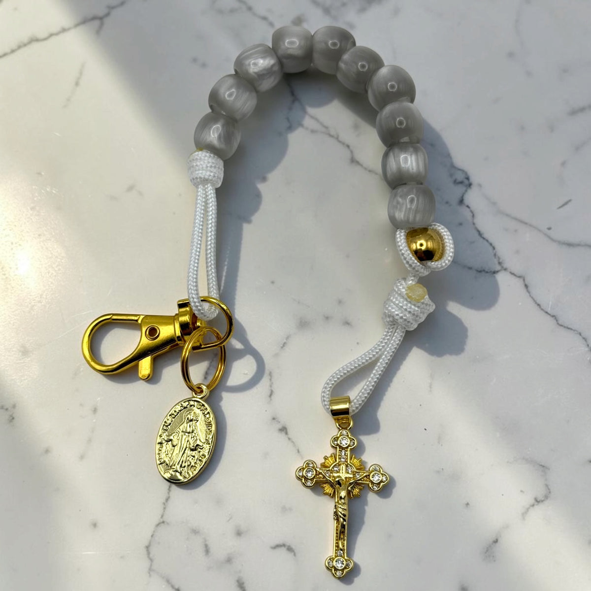 Gray decade rosary with white cord, gold-tone hardware, Marian medal, and crystal crucifix