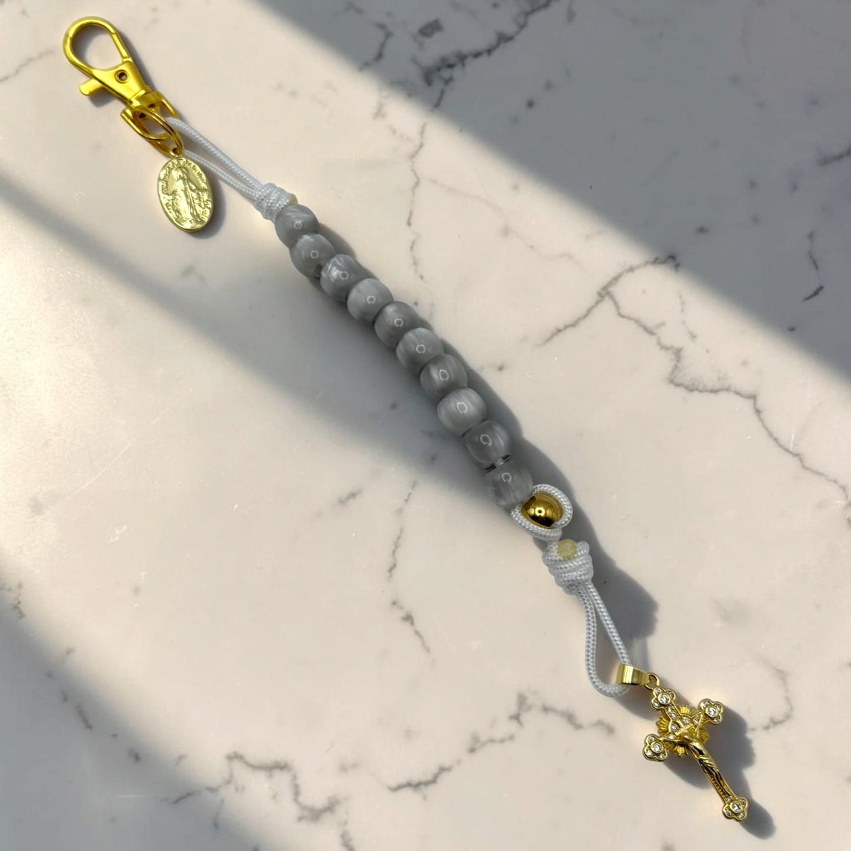 Full-length gray decade rosary with white cord, gold-tone Marian medal, lobster clasp, and crystal crucifix