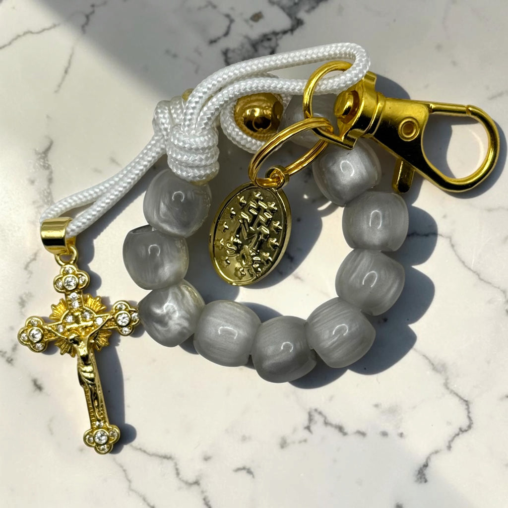 Close-up gray decade rosary with glossy gray beads, white cord, gold-tone Marian medal, lobster clasp, and crystal crucifix